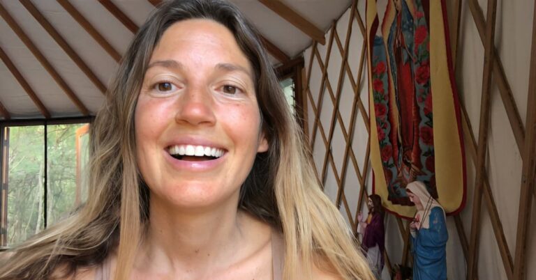 Sarah smiling inside a yurt with lattice walls and colorful fabric decorations.